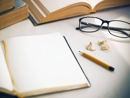 On the white table there are old books, an open diary with a yellow bookmark for notes, shavings...