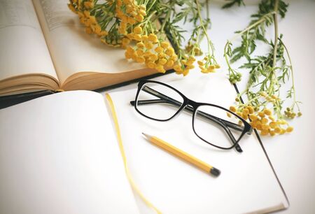A workplace where on a white table with books for learning black-rimmed glasses, a pencil and a...