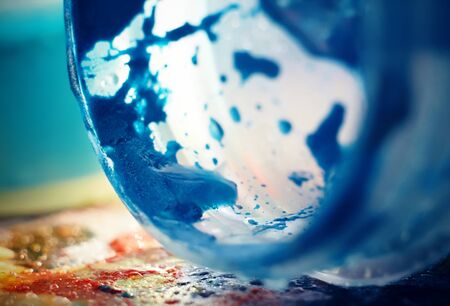 A jar of bright shiny blue gouache paint fell on its side on a multi-colored palette illuminated by sunlight. A mess during the creative work.の写真素材
