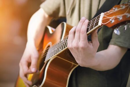 The guy in the green hoodie plays a bright orange acoustic six-string guitar, holding the chords....