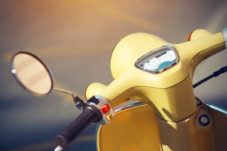 The steering wheel of a vintage yellow moped with a rear-view mirror and a speedometer, which stands on the road with yellow markings, illuminated by light.の写真素材