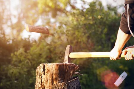 A man in black sports clothes cuts a sharp ax log, parts of which are scattered into chips,...