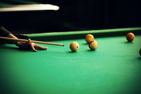 A woman in a green sweater holds a cue and aims at a billiard ball, which is among the other balls...