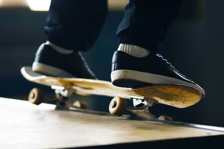 On a yellow skateboard, a guy in black sneakers with blue laces and black pants performs a trick on the rampの写真素材