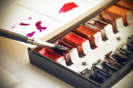From the palette with different colors of watercolor paints wet brush scoops Burgundy paint to paint her picture.の写真素材