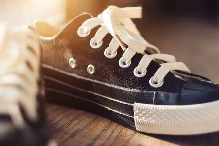  Black fashionable new sports sneakers with white laces stand on the wooden floor, illuminated by the summer sunlight.の写真素材