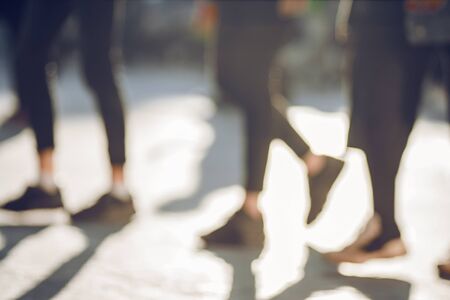 A blurred abstract background of the feet of young people walking on the sidewalk, which are illuminated by bright light and cast long dark shadows.の写真素材