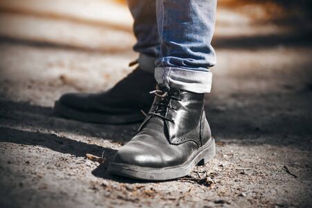 A man in blue jeans and black elegant leather shoes stands on a sandy road in a Park on an autumn...