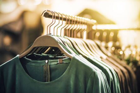 On hangers in the clothing store hang fashionable green dresses, illuminated by artificial light.の写真素材