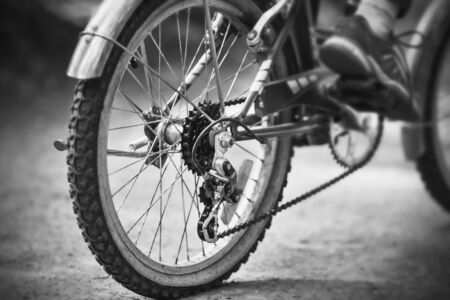 A black-and-white image of the rear wheel of a high-speed sports bike, on which a man in sports shoes is riding fast on a park road.の写真素材