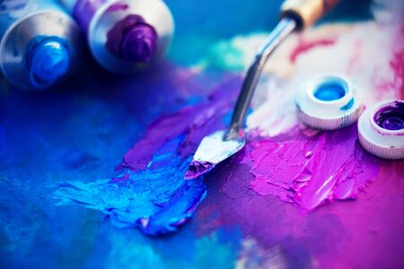 Tubes of blue and purple oil paint lie on a palette, along with a thin palette knife that mixes the two colors.の写真素材