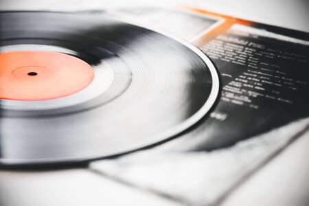 A black retro vinyl record with music recorded on it lies on the paper cover of the music album.