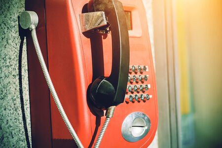 Street retro red vending machine with phone, illuminated by bright sunlight.の写真素材