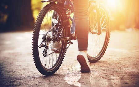A speed sports bicycle on which a girl is sitting in the middle of a Park path is illuminated by the bright light of the summer sun. Sports recreation.の写真素材