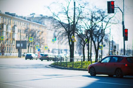  A city intersection where a red car stopped at a turn near a traffic light that is lit red. It's...