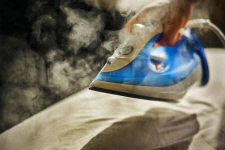 The man is holding a new blue modern iron in his hand and is about to steam a beige crumpled fabric...
