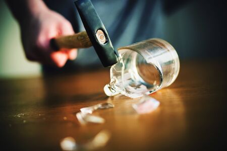 The man smashed a glass mug with a hammer, which shattered when the sharp shards hit the wooden table. Dangerous prank.の写真素材