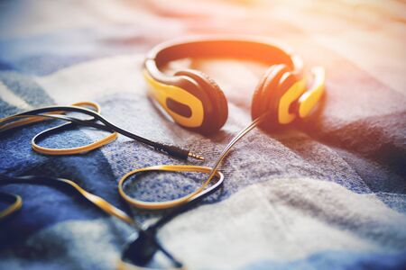 Yellow headphones with a microphone lie on a blue plaid blanket, illuminated by bright sunlight. Music and inspiration.の写真素材