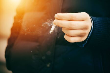 A man in a blue warm jacket smokes a cigarette in the wintertimeの写真素材