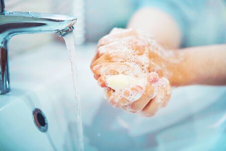 A man carefully washes his hands with soap and thick foam in the bathroom over the sink, from the tap of which water flows.の写真素材