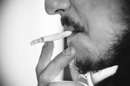 A black-and-white image of a man Smoking a cigarette, his beard illuminated by sunlight.の写真素材