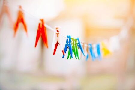 On a bright Sunny day, colorful bright clothespins hang on a long white clothesline, waiting for wet...