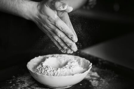 Black-and-white image of the process of cooking homemade dough. The cook mixes the flour with the...