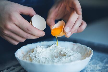  A man has broken the shell of a chicken egg and is about to pour it into a bowl of flour to make dough. Home cooking.の写真素材