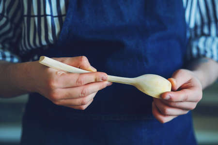 A man in a blue apron and striped shirt is holding a beautiful hand-carved wooden spoon.の写真素材
