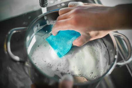 A man washes a pot in the kitchen sink with a blue sponge and thick foam. Household chores. Kitchen utensils.の写真素材