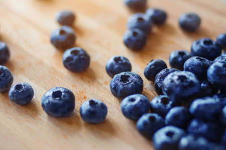 On the kitchen wooden board lie large ripe washed berries of forest blueberries, illuminated by sunlight. Rich harvest.の写真素材