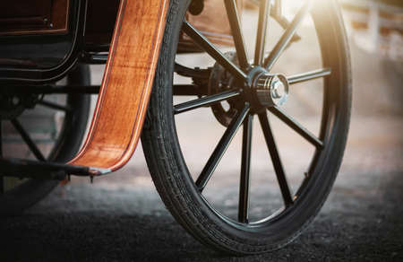 A dark large wheel on an ancient carriage with wooden elements for horses, which is illuminated by rays of sunlight. History.の写真素材