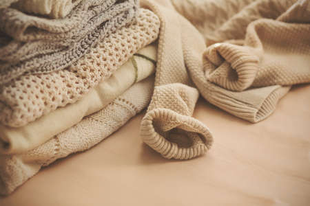 Several warm, soft, patterned sweaters are stacked, and next to them is another one with the sleeves...