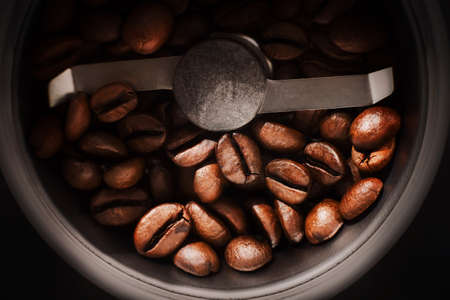 Top view of roasted aromatic coffee beans lying between the blades in a coffee grinder. The process of making coffee. Macro.の写真素材