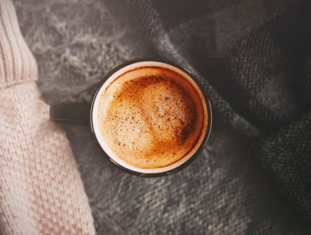 Top view of a black mug of hot, aromatic cinnamon coffee, which is set among warm wool sweaters. Hygge. The cold season and the hot drink.の写真素材