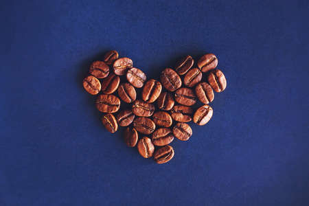 Top view of the heart symbol, lined with fragrant roasted coffee beans, lying on a blue background....