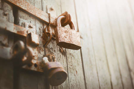 An old rusty lock hangs on the old painted gate, closing it, illuminated by sunlight. Secret. An...