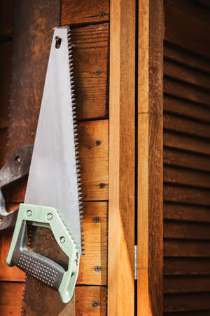 A new hand saw hangs on a wooden wall in a village workshop next to old rusty saws, illuminated by sunlight. Tools and rural life.の写真素材