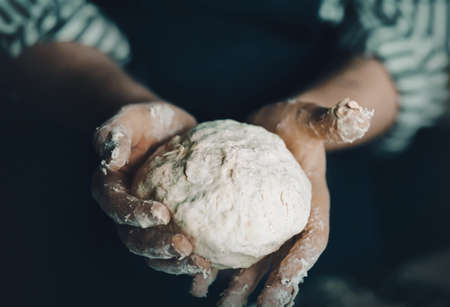A male chef in a dark blue apron holds a pastry dough in his hands. Home cooking. Traditional pizza recipe. Delicious food.の写真素材