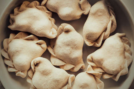 Top view of delicious frozen homemade dumplings that lie in a large plate. Dough with various fillings inside. Frozen semi-finished products. Russian cuisine.の写真素材