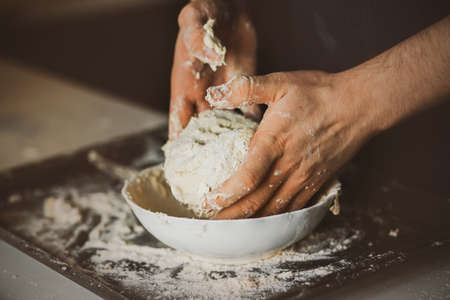 A male cook kneads dough in a plate with his hands. Home cooking. The process of making dough for...
