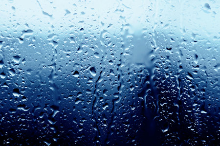 Raindrops fall on the transparent window glass during a downpour on a cold autumn day. Cloudy wet sad weather. Water. Melancholy.の写真素材