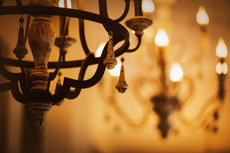 On the old and elegant chandeliers, lamps in the form of candles glow in the evening twilight. Decorative luxury lighting of the room. A palace or a hotel.の写真素材