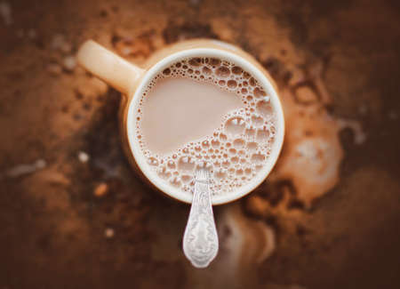 Top view of a beige mug with warm delicious cocoa with milk and a silver teaspoon. Spilled cocoa and a mess in the kitchen. A nice drink in the morning.の写真素材
