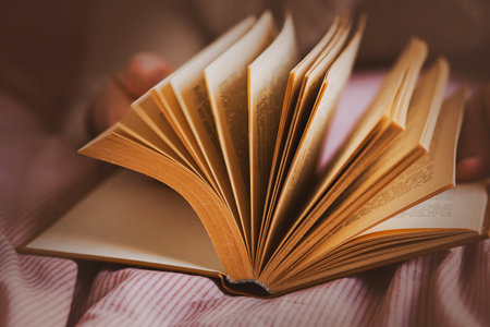 A man, lying on a soft bed, flips through the pages of a thick, interesting old book. Relaxing while reading a novel. Self-development.の写真素材