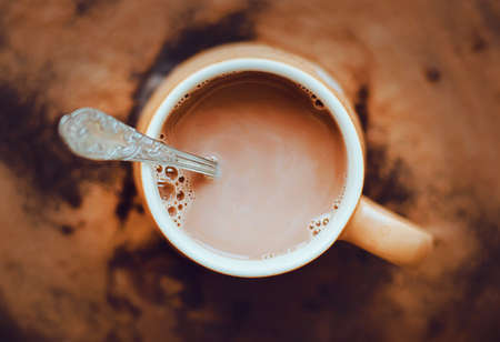 Top view of a beige mug with warm delicious fragrant cocoa with milk and a silver teaspoon in it. Nice breakfast. Coffee with milk in the morning.の写真素材