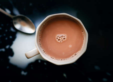 Top view of a gray cup of warm natural fragrant cocoa, next to which lies a silver teaspoon and spilled milk. Delicious drink for breakfast.の写真素材