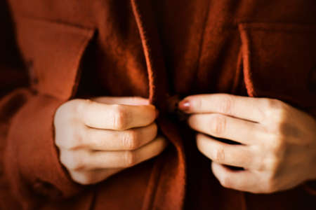 A woman with a brown manicure, dressed in a ginger warm cozy shirt, is buttoning her buttons. Casual fashionable clothes for the autumn season. Soft focus.の写真素材