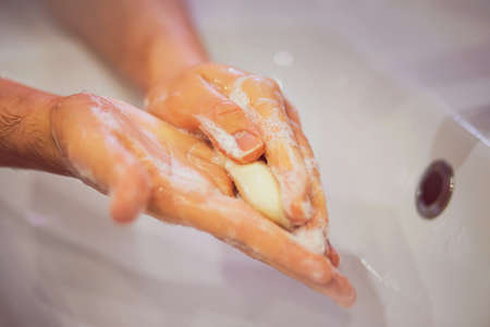 A man carefully washes his hands with white soap over a white ceramic sink in the bathroom. Cleanliness and hygiene.の写真素材