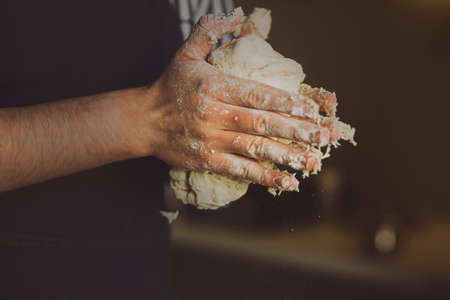 A man in a blue apron holds fresh wheat dough for baking in his hands. The process of preparing the dough. Home cooking.の写真素材